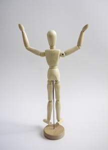 A wooden mannequin figure raising its arms in a gesture of success on a neutral grey background.